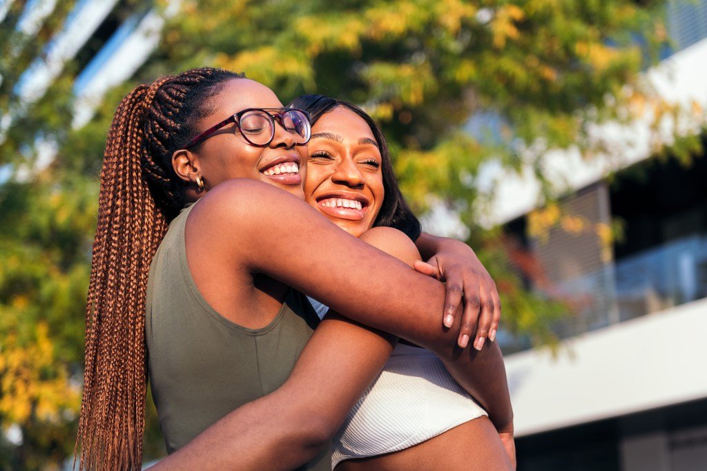 Two young women hugging each other fortunately and smiling.