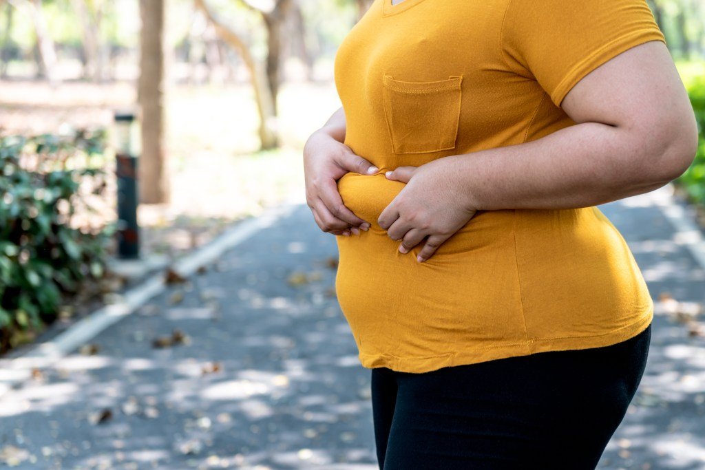 A woman carrying excess fat around her waist in a park, related to obesity and health care