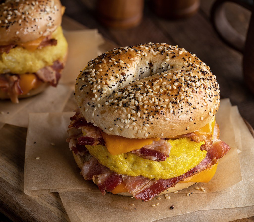 Breakfast bagel sandwich with bacon, egg and cheddar cheese on a rustic wooden table
