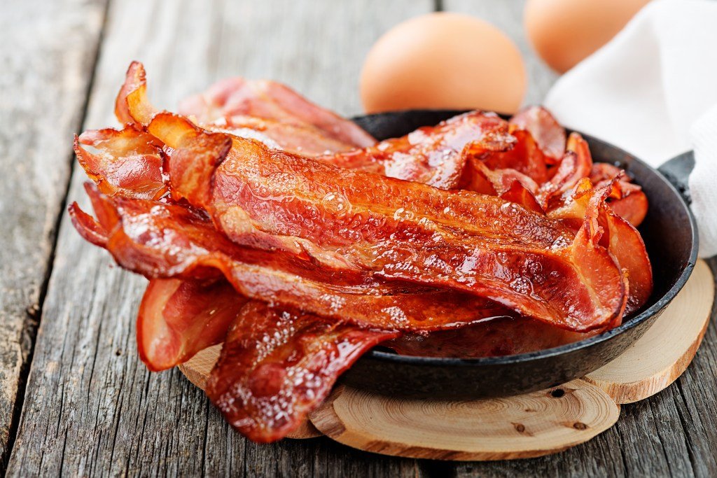 Top view of hot fried bacon pieces in a cast iron skillet on a wooden surface