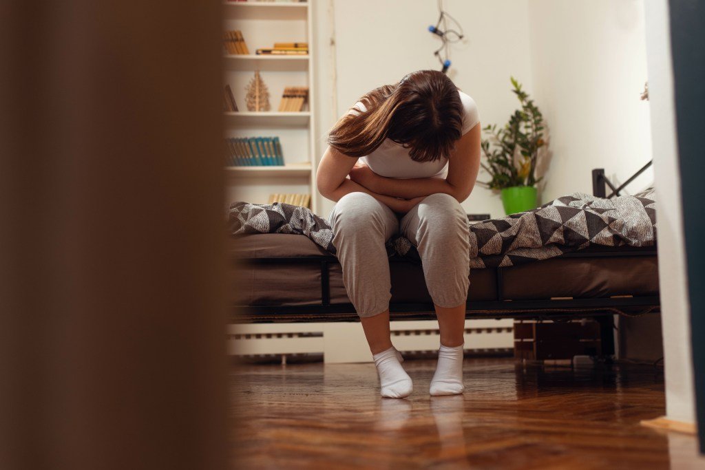 Young woman experiencing abdominal pain while sitting in bed due to menstruation