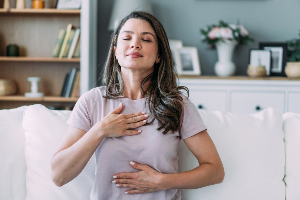 A woman holds her chest while inhaling deeply.