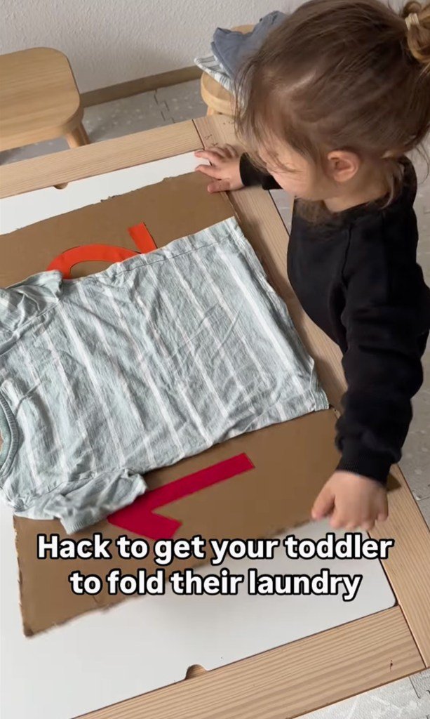 A baby learning to fold clothes using a home cardboard tool