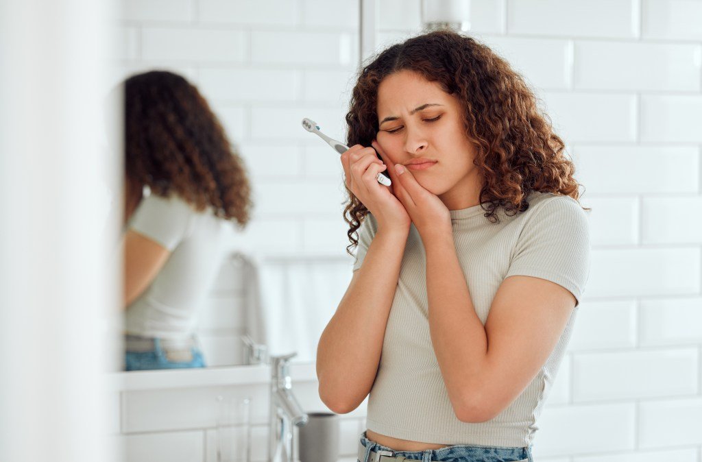 A woman fights a toothache while brushing her teeth.