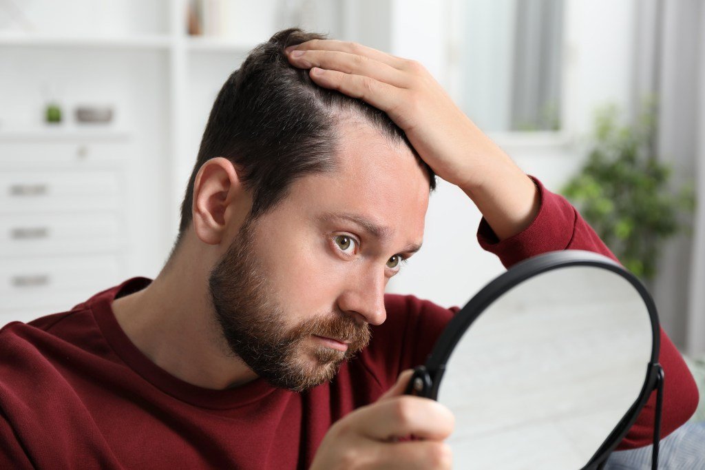 Man with the problem of losing hair by examining his reflection in a home mirror
